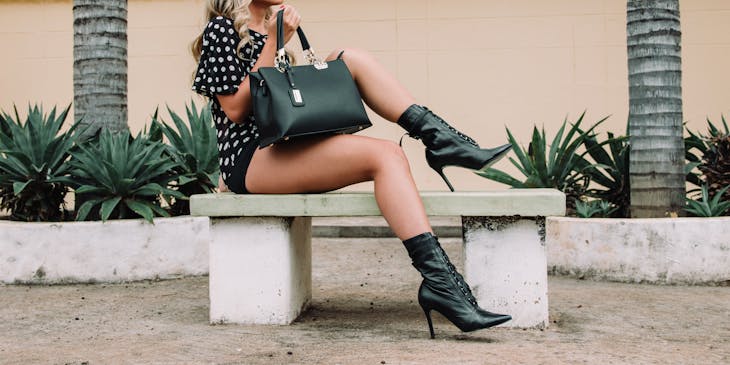 Una mujer usando ropa de una marca de moda con gafas de sol y un gran bolso de cuero negro sentada en un banco.