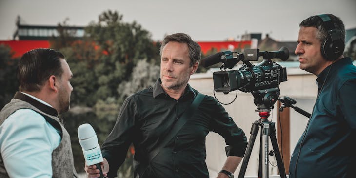 reporter with microphone interviewing man in front of camera