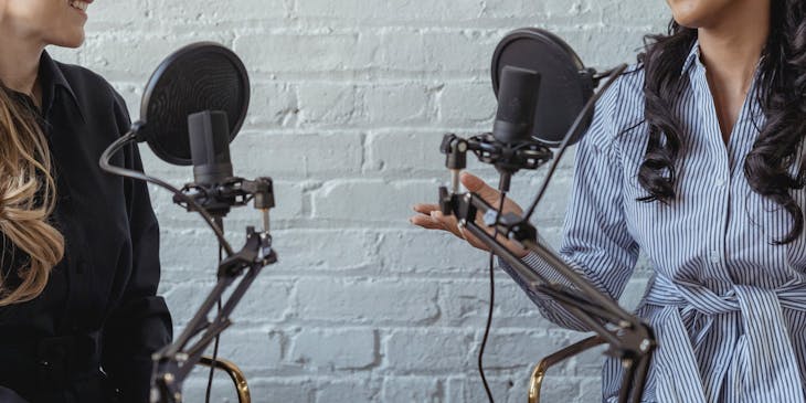 Two women talking in front of microphones and recording a podcast.