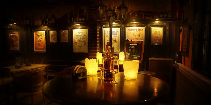 Mesa redonda en un restaurante irlandés con velas, vasos y una botella de whisky irlandés en la parte superior y carteles de compañías de licores en las paredes al fondo.