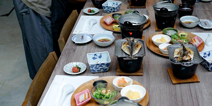 Table laid out with bowls, grilled fish, and side dishes with a waitress leaning over the table.