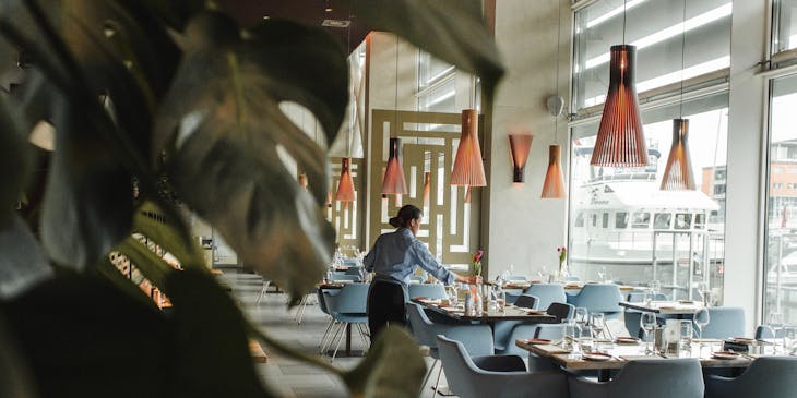 Espaço interno de um restaurante europeu com uma mulher sentada em uma das cadeiras.