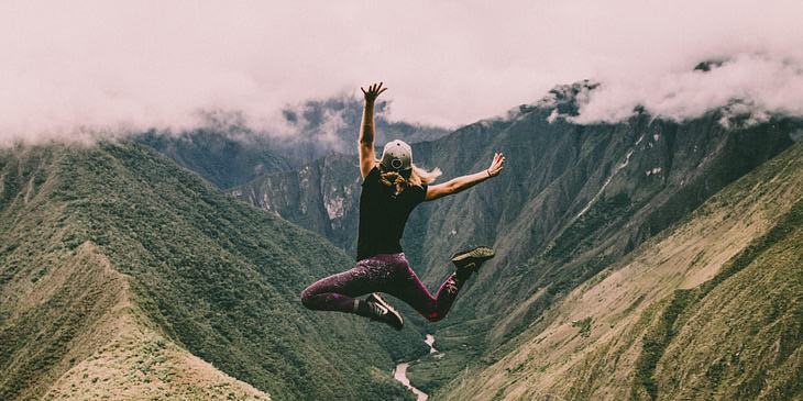 Una mujer saltando energéticamente en medio de unas montañas verdes