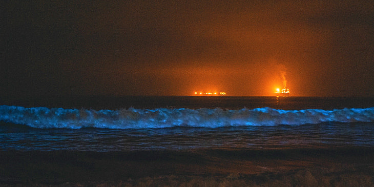 Olas del mar con brillo azul bioluminiscente en la noche con luces de barcos de agencias de tours en bahías bioluminiscentes al fondo