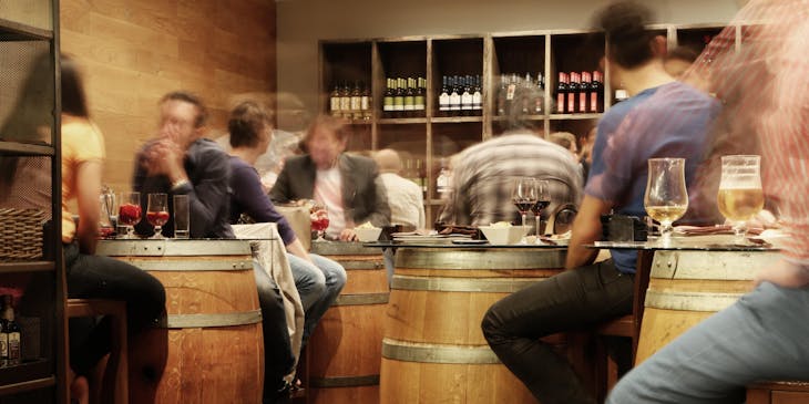 Clientes sentados alrededor de barriles como mesas, bebiendo copas de vino en un bar de chiquiteo.