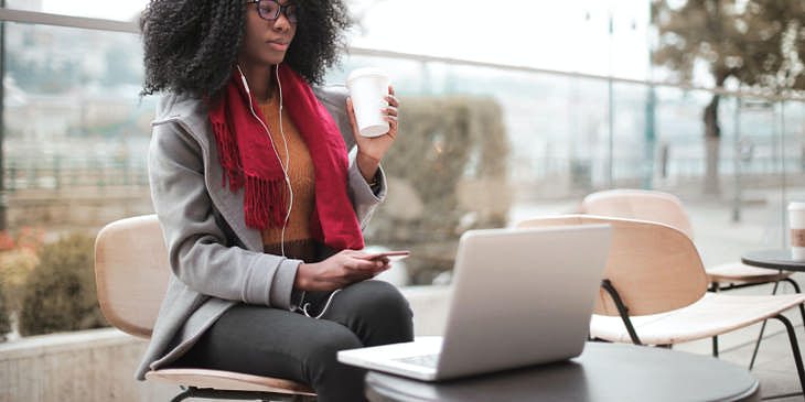 Una mujer tomando café y usando una laptop en un café Internet.