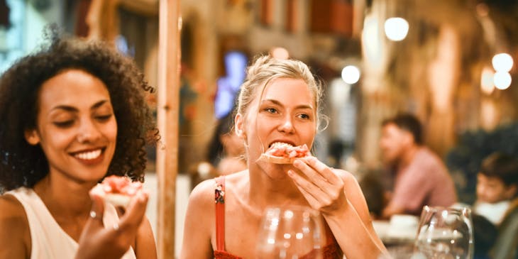 Dos mujeres tomando vino blanco y comiendo aperitivos en un centro botanero.