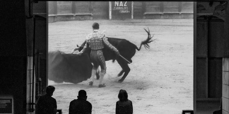 Tres personas analizando un video de un torero en el ruedo en un negocio de cursos de tauromaquia.