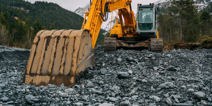 Una excavadora sobre un suelo rocoso con un bosque de fondo en una empresa de maquinaria pesada.