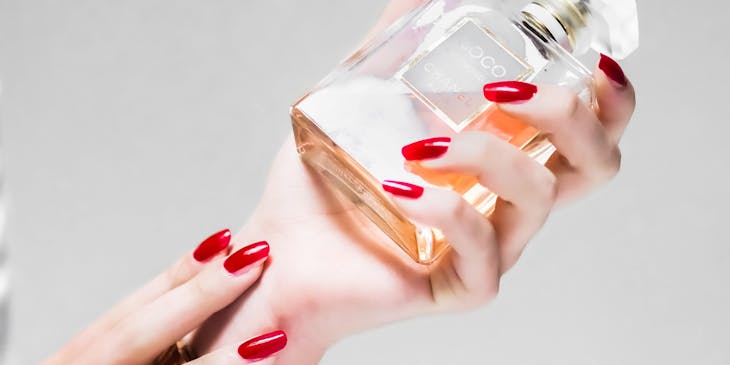 Una mujer con manicura color rojo sosteniendo un perfume en una empresa de perfumes.