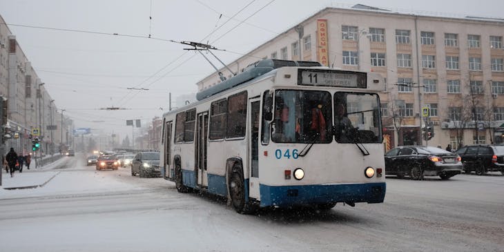 Un trolebús blanco y azul transitando por una ciudad nevada.