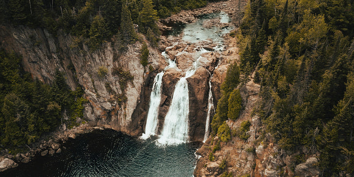 La vista desde arriba de tres cascadas y un lago abajo con pinos alrededor en un viaje ecológico de una empresa de viajes ecológicos.