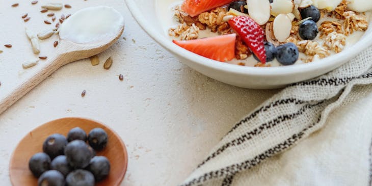 Una mesa de desayuno con varios alimentos, como una toronja, un jugo de toronja, moras azules y un plato de yogurt con granola y frutas de temporada en una empresa de yogurt.