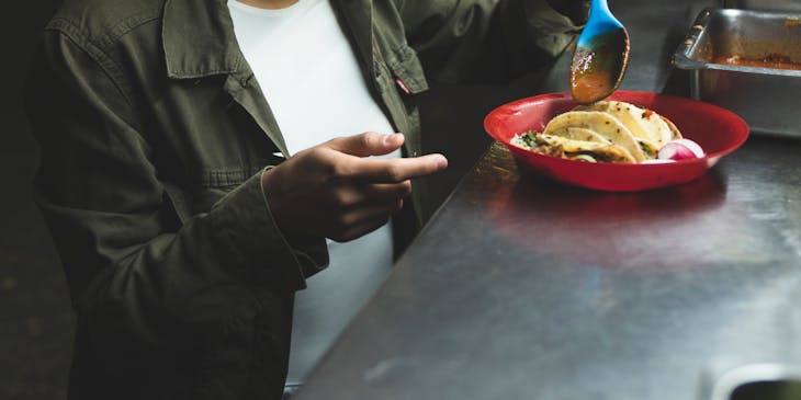 Una mujer que pone salsa a un plato con tacos en un food truck de tacos.