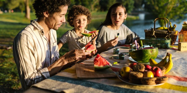 Una familia comiendo fruta en un merendero al aire libre.