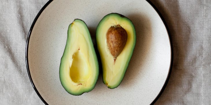 Un aguacate partido en dos sobre un plato de cerámica blanco sobre un mantel blanco en una mesa de un negocio de aguacate.