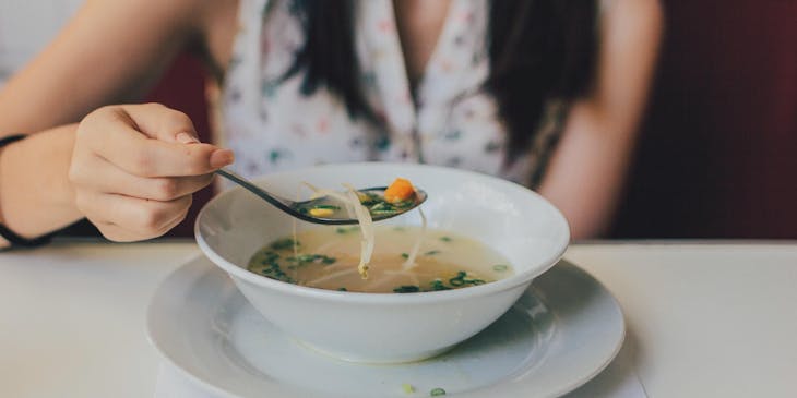 una mujer tomando una cucharada de ajiaco en un plato hondo en un negocio de ajiaco