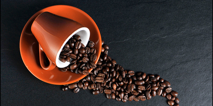 Taza color naranja acostada sobre un plato del mismo color con granos de café derramados sobre una superficie de piedra oscura en un negocio de café hondureño.