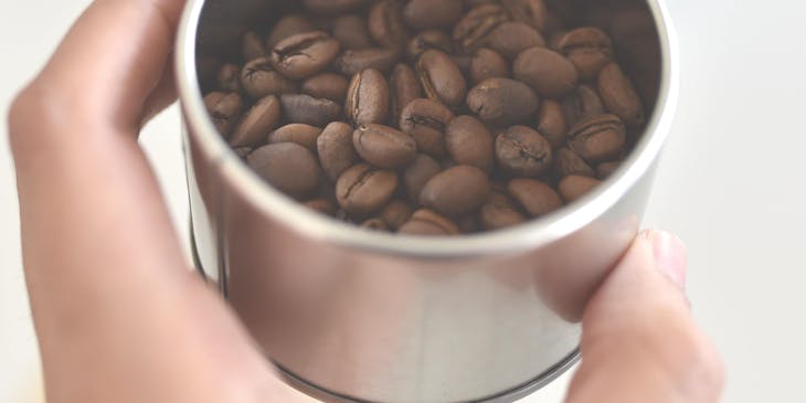 Mano de mujer sosteniendo un recipiente con café colombiano en su interior sobre un fondo blanco.