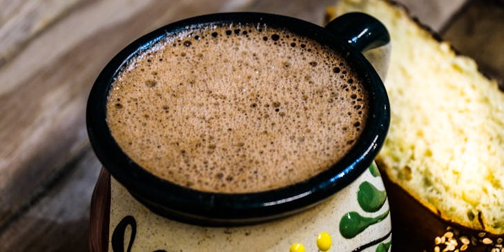 Champurrado de chocolate en una taza mexicana acompañado por una rebanada de pan dulce en un negocio de champurrado