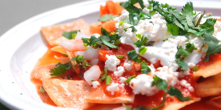 Chilaquiles rojos con queso y cilantro en un plato blanco en un negocio de chilaquiles