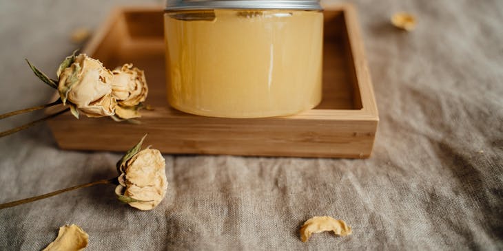 Un envase con crema de miel en una superficie de madera con flores marchitas de adorno en un negocio de cremas naturales.