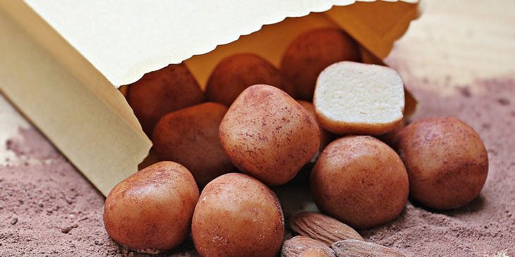 Bolitas de mazapán cubiertas de chocolate saliendo de una bolsa café y sobre polvo de cacao en un negocio de dulce de mazapán.