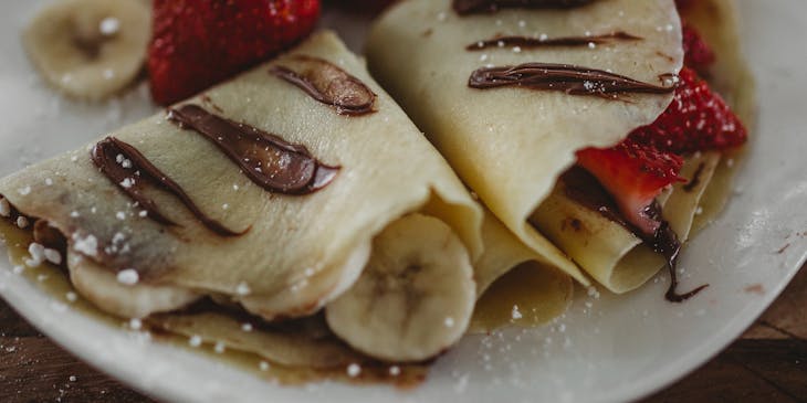 Crepas dulces sobre un plato con trozos de plátano y fresas en un negocio de gusgueras.