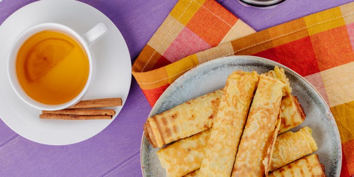 Marquesitas sobre plato gris en fondo morado junto a una taza de té de canela en un negocio de marquesitas