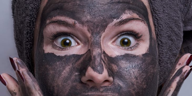 Una mujer sorprendida con una toalla en la cabeza y una mascarilla de carbón activado en el rostro en un negocio de mascarillas.