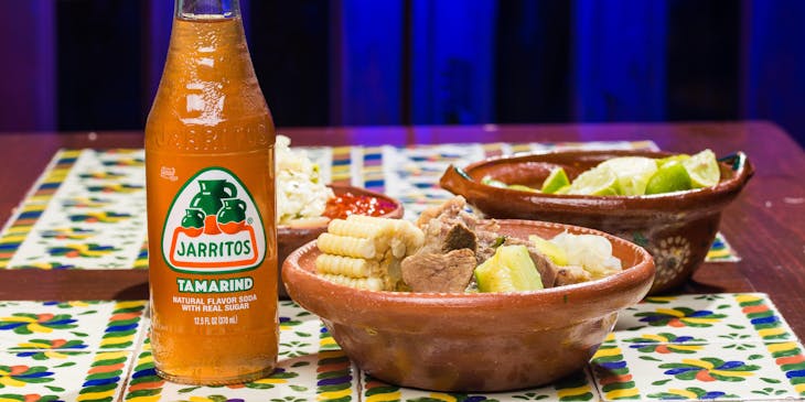 Mondongo en una cazuela de cerámica a un lado de un refresco de naranja de jarritos en un negocio de mondongo.