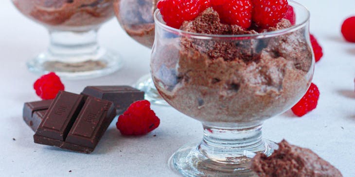 Tres copas rellenas de mousse de chocolate con un par de frambuesas encima y unos trozos de cacao a un lado en un negocio de mousse.