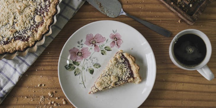 Una rebanada de pastafrola sobre un plato de cerámica blanco a un lado de una pastafrola entera sobre una mesa de madera en un negocio de pastafrola.