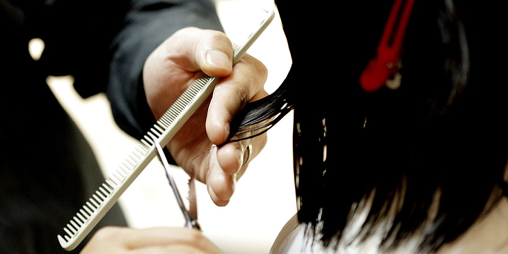 Hombre cortando el pelo a una mujer en un negocio de peluquería a domicilio.