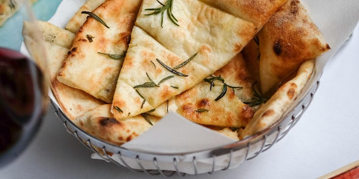 Una charola de pan pita con especias mediterráneas en el centro de una mesa en un negocio de pitas.