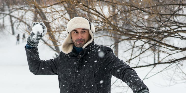 Un hombre lanzando una bola de nieve afuera de un negocio de ropa para invierno