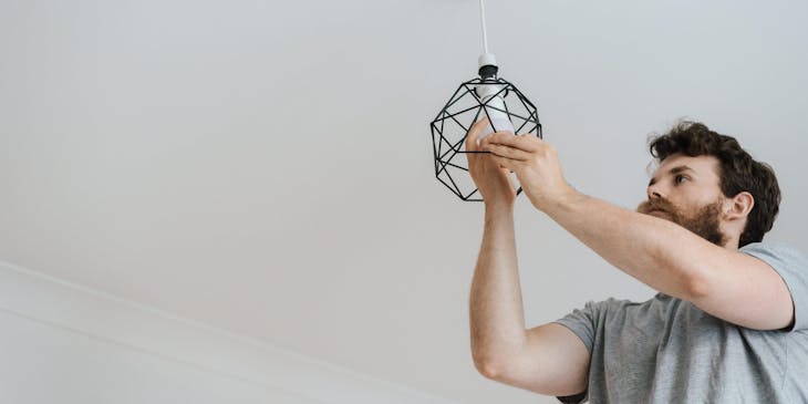 Um homem fazendo um serviço residencial instalando um lustre.