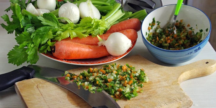 Una tabla de madera con sofrito recién hecho a un lado de un bowl lleno de sofrito en un negocio de sofrito.