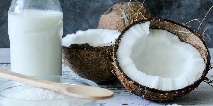 Un coco partido a la mitad junto a un bote de leche de coco y un plato con coco en polvo en un negocio de tembleque.