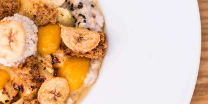 Varios tostones servidos sobre una cama de avena en un plato hondo color blanco sobre una mesa de madera en un negocio de tostones.