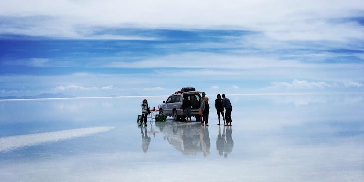 Vista del gran Salar de Uyuni con turistas de un negocio de tours a Uyuni en una camioneta y el efecto espejo en el suelo.