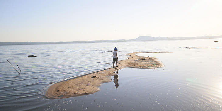 Mujer caminando con una caña de pescar sobre un estrecho de tierra en medio del lago Ypacaraí en un negocio de tours al Lago Ypacaraí.