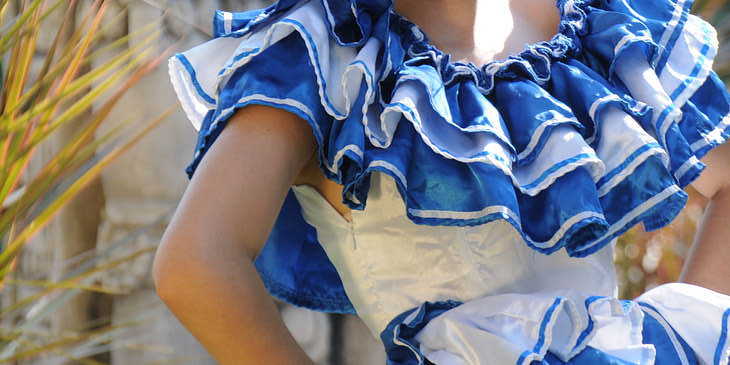 Mujer vistiendo un traje típico de Honduras con una escultura Maya y vegetación de fondo en un negocio de trajes típicos hondureños.