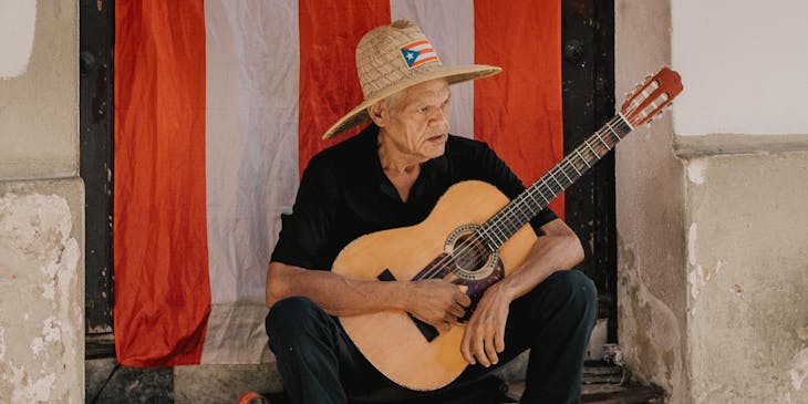 Un hombre con una guitarra frente a una bandera de Puerto Rico en un negocio de trifongo.