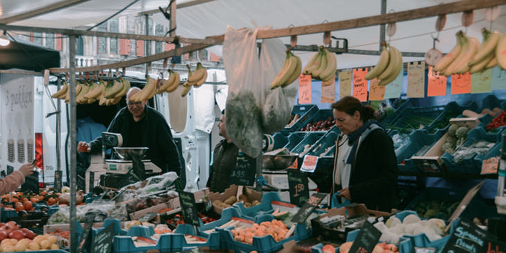 Tres personas en el interior de una verdulería con gran variedad de frutas y verduras exhibidas.