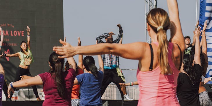 Grupo de personas practicando zumba al aire libre frente a sus instructores.