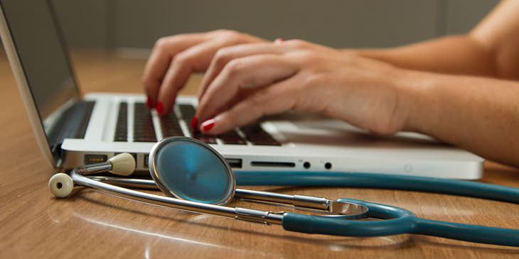 Manos sobre un teclado de una computadora y un estetoscopio al lado, en una págna de medicina.