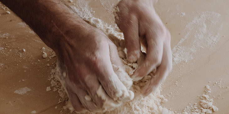 Manos de panadero amasando masa sobre una base de madera en una panadería de pan de la arena.