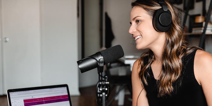 Una mujer con audífonos y un micrófono en una sala grabando un podcast en su computadora.