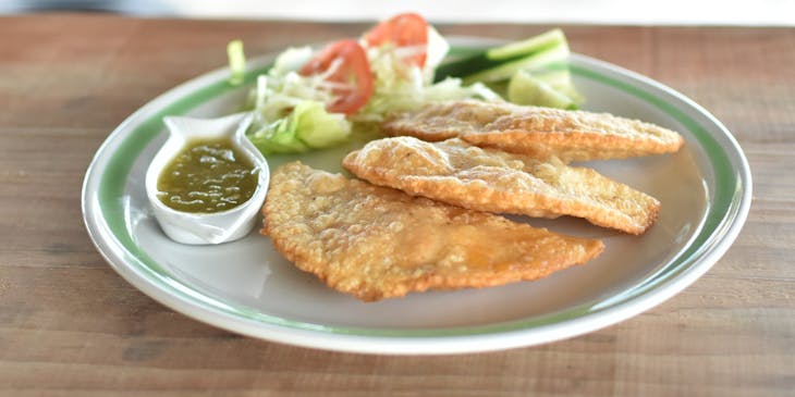 Un plato con tres pescadillas, ensalada y salsa sobre una mesa de madera en un puesto de pescadillas.